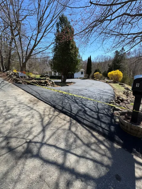 Curved gravel driveway with leafless trees, shrubs, and a white building under a clear blue sky
