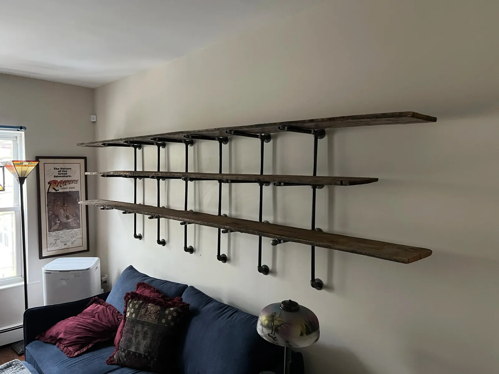 Three rustic wooden shelves supported by black metal pipes mounted on a white wall in a living room.