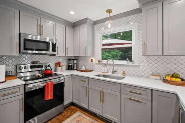 Gray kitchen with stainless steel appliances, white countertops, and gold hardware.