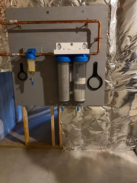 Whole-house water filtration housings and copper piping mounted on a board in a basement