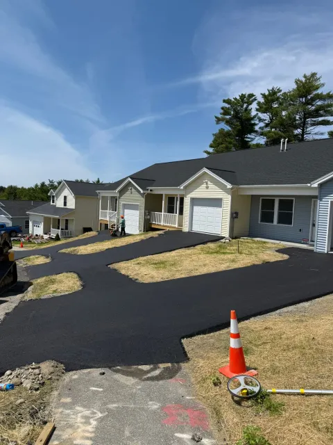 Newly paved black asphalt driveways connecting to garage entrances of light-colored suburban houses under a blue sky.