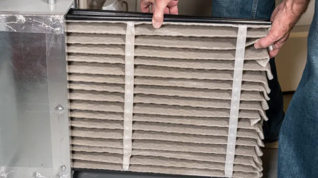 Person replacing an air filter in a heating or cooling unit.