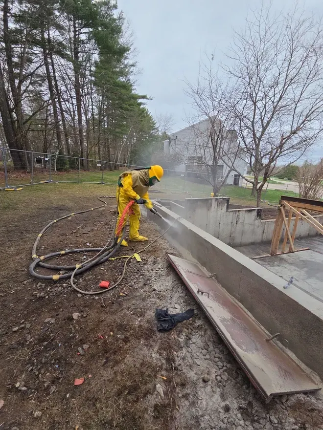 Worker spraying a house wall with a power sprayer outdoors.
