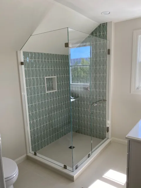 Modern bathroom with glass-enclosed shower featuring geometric patterned tiles, alongside a white toilet and a window.