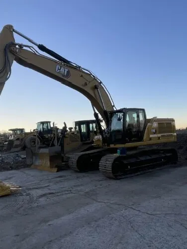 A large excavator and other heavy construction equipment are staged on a cleared worksite under a clear sky.