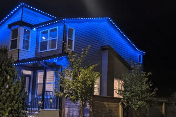 House illuminated with blue permanent lighting along the roofline and window frames, creating a modern, festive atmosphere at night.