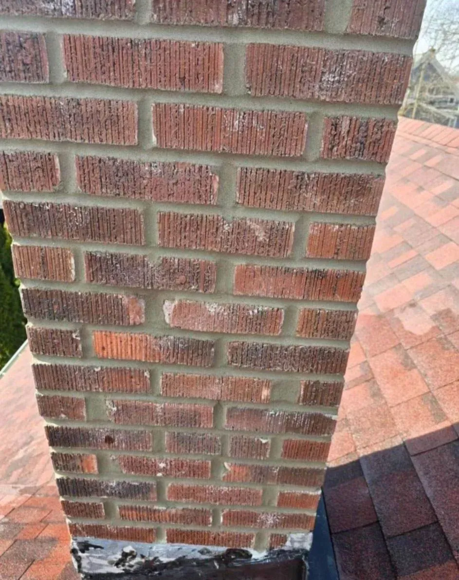 Brick chimney on a red shingled roof, showing mortar and base flashing.