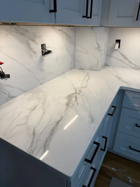 Modern kitchen with white marble-look countertops and backsplash, blue-gray cabinets, and wood flooring