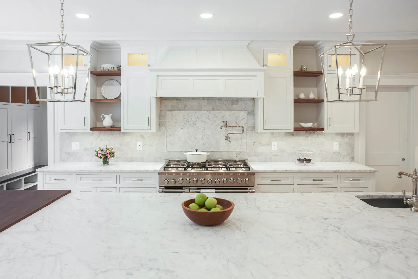 Custom white kitchen with marble countertops, glass-front cabinets, lantern pendant lights and a professional gas range