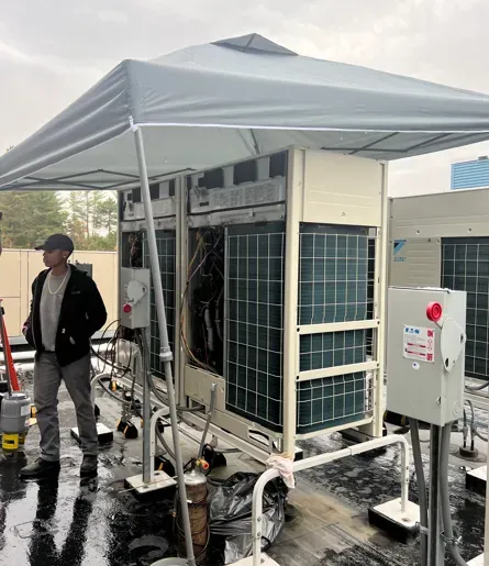 Outdoor HVAC unit under a white canopy on a wet rooftop, with a worker standing nearby.
