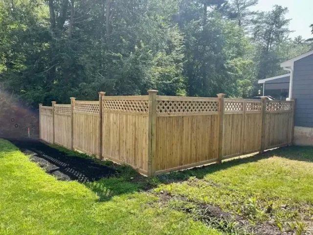 Wooden privacy fence with lattice top in a sunny backyard beside a house and trees