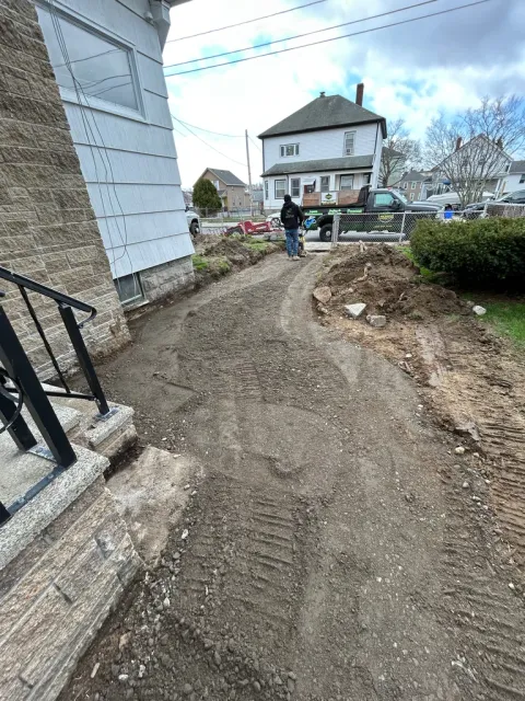 Residential construction site with dirt pathway between houses, workers visible, and clear sky