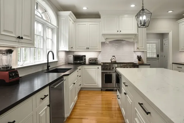 Modern kitchen with white cabinets, black countertops, stainless appliances, and a central island with marble surface.