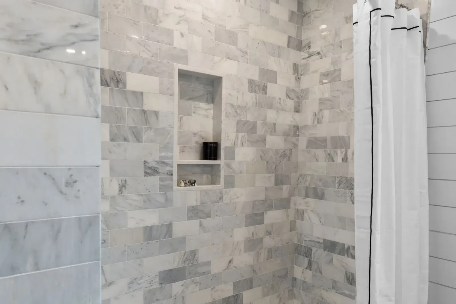 Marble-tiled shower with recessed shelves and a white shower curtain