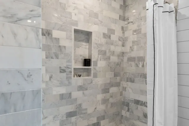 Marble-tiled shower with recessed shelves and a white shower curtain