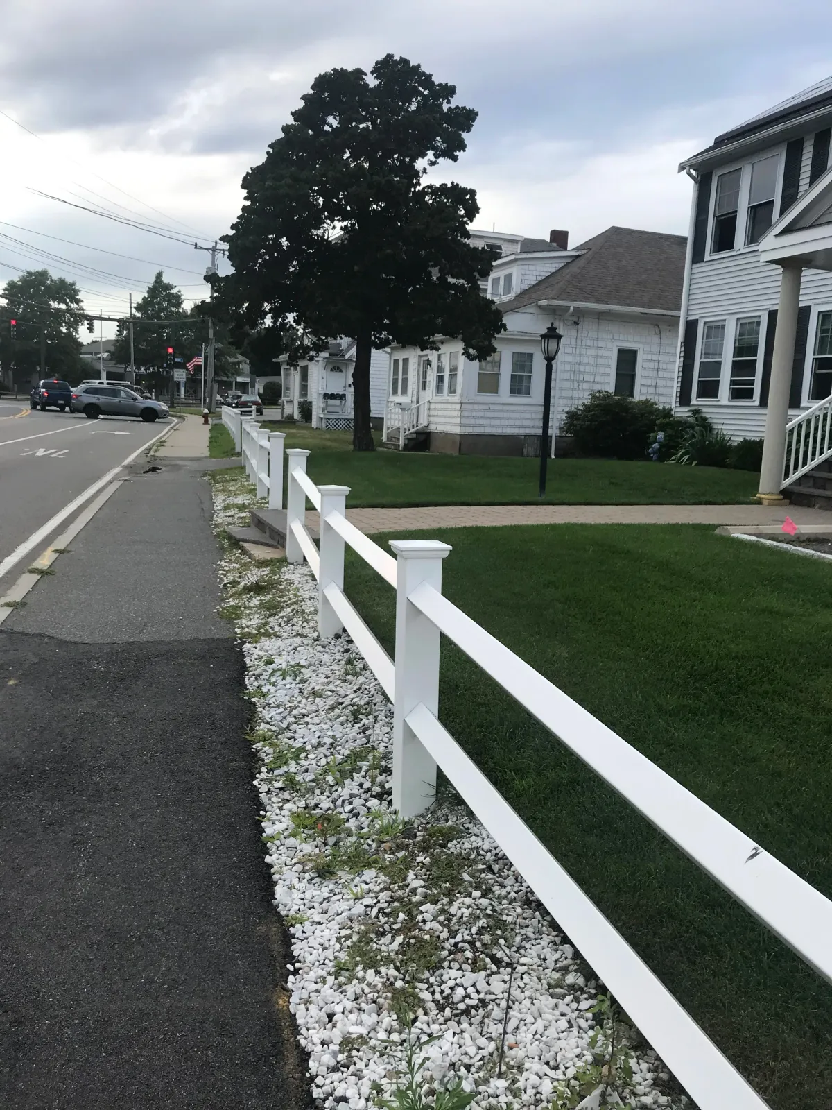 Residential street with white fence, houses, and trees