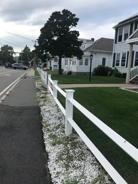 Residential street with white fence, houses, and trees