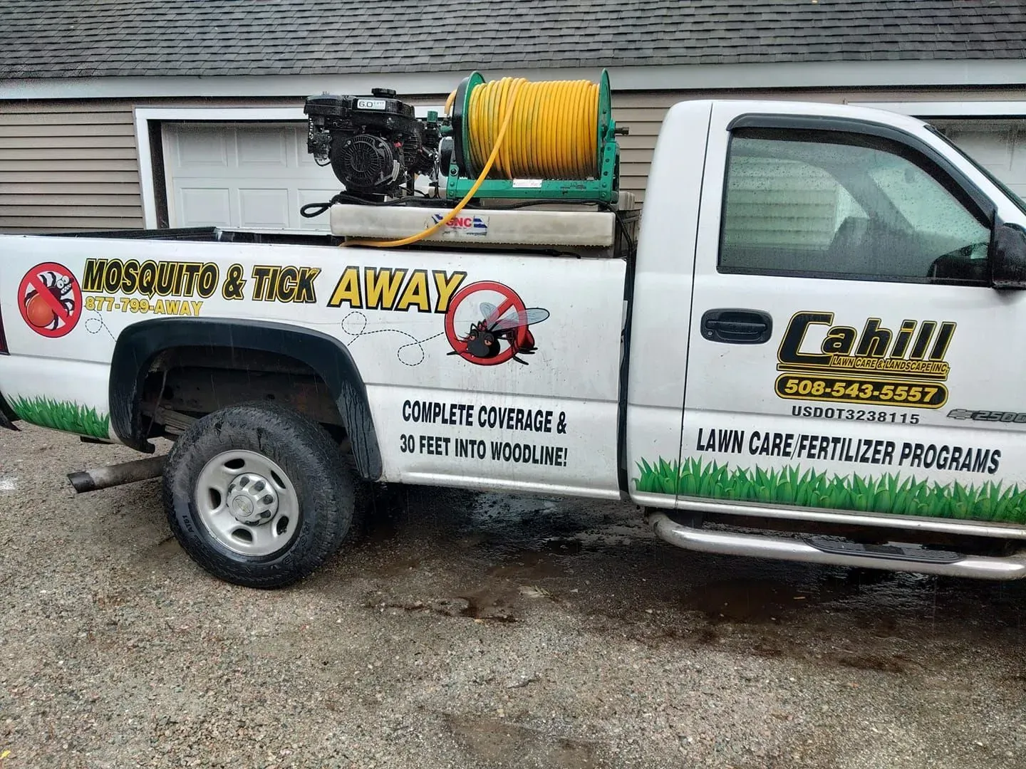White utility pickup with pest-control branding and hose reel parked by a garage.