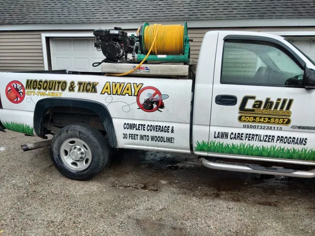 White utility pickup with pest-control branding and hose reel parked by a garage.