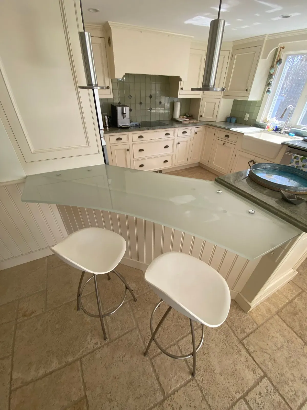 White bar stools at a glass-topped counter in a cream-colored kitchen.