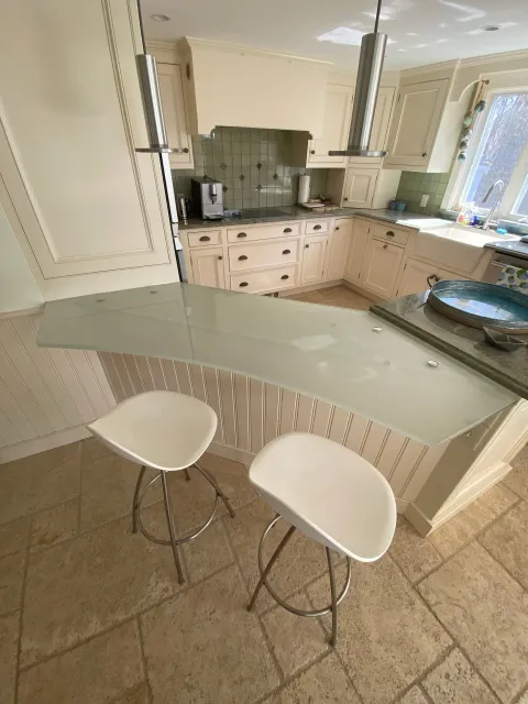 White bar stools at a glass-topped counter in a cream-colored kitchen.