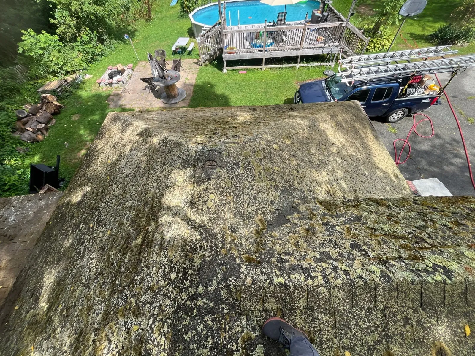 Steep mossy roof seen from above, with a blue pool and a driveway with a truck nearby.