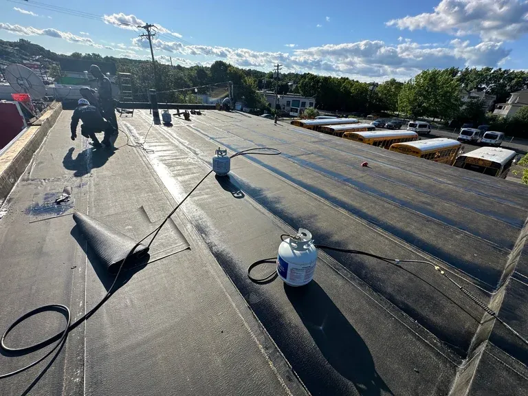 Workers applying waterproof membrane coating to a flat commercial roof during daytime construction