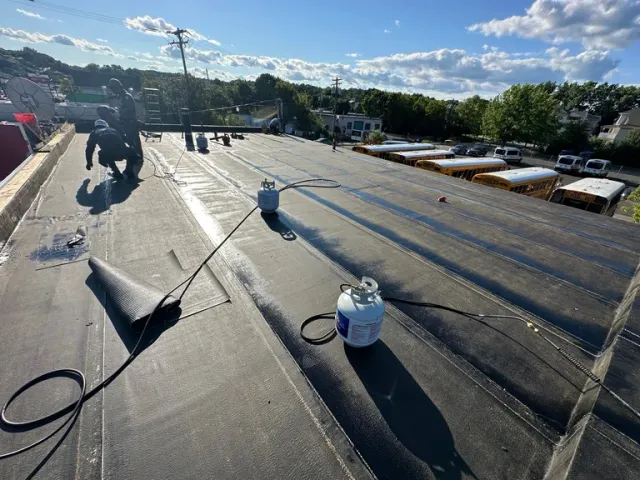 Workers applying waterproof membrane coating to a flat commercial roof during daytime construction