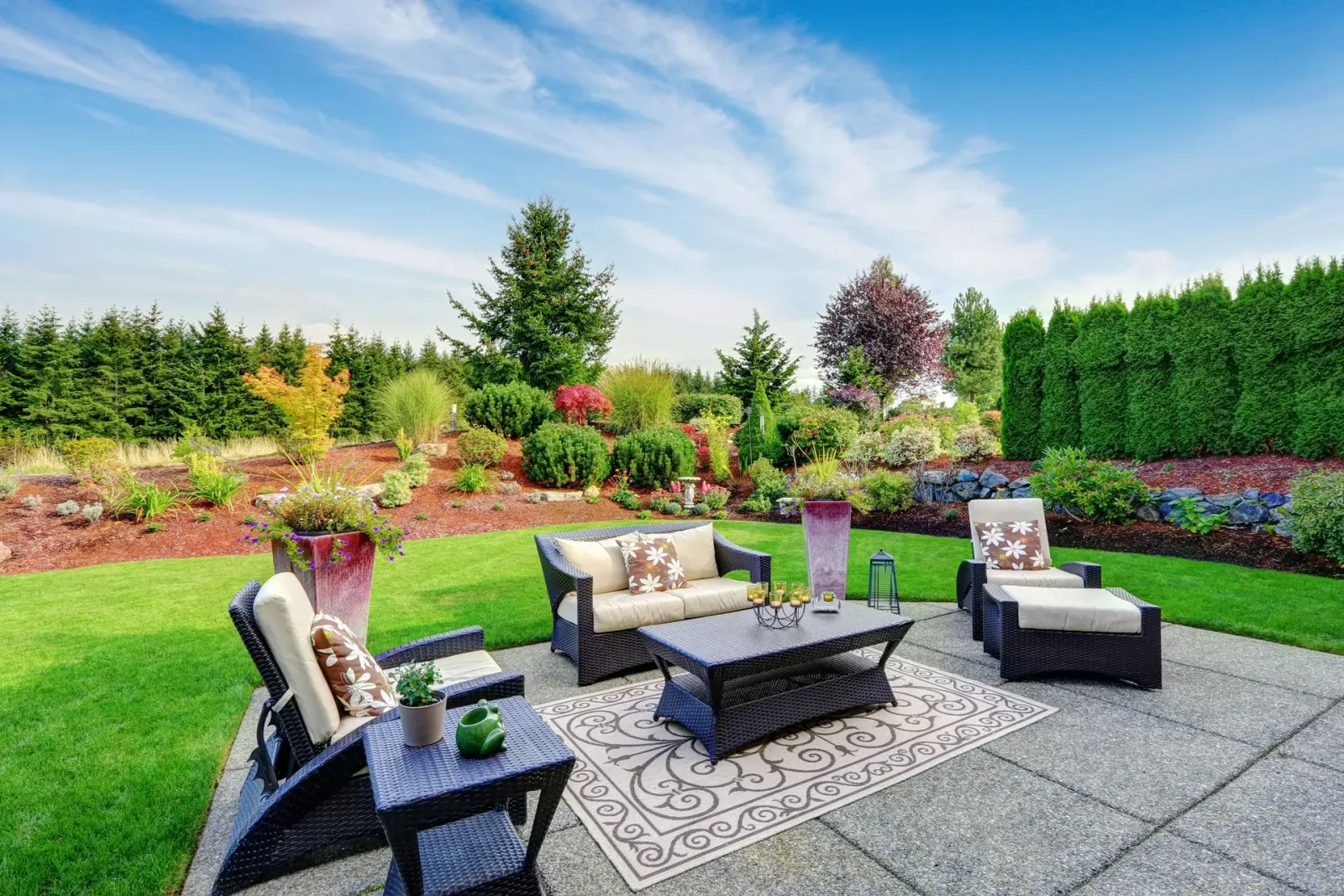 Patio furniture set with a sofa, chairs, and table on a stone patio overlooking a landscaped backyard and blue sky.