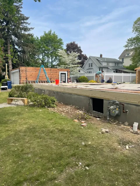 Custom home foundation and floor framing in Wakefield, MA, with construction workers, wooden framing, and a partially completed structure in a residential setting.