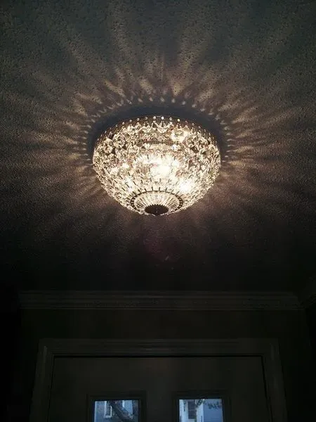 A sparkling crystal ceiling light casts a starry pattern on the ceiling above a door.