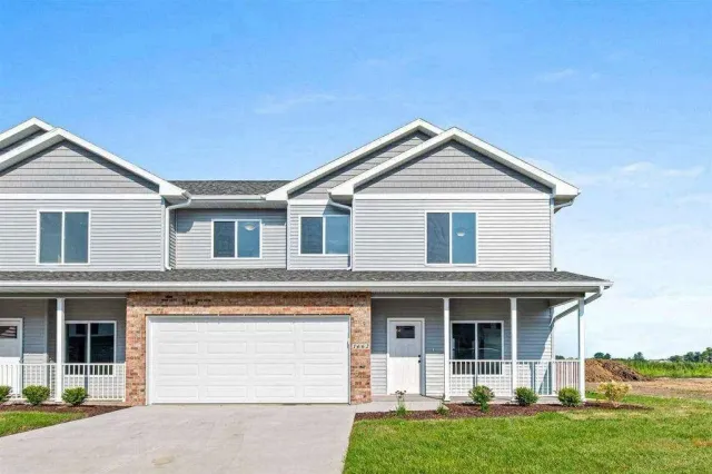 A white house with a white garage door is sitting on top of a lush green field.