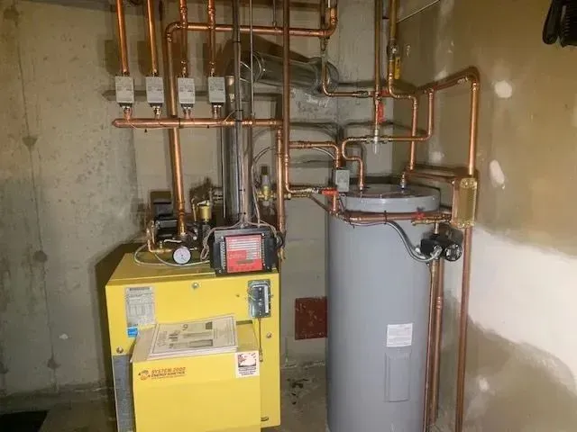 Boiler room with yellow furnace, gray water heater, and exposed copper pipes on concrete walls