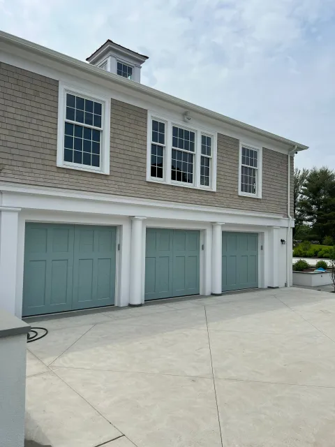 Three-car garage with light blue doors and windows above, light brown siding, and white trim.