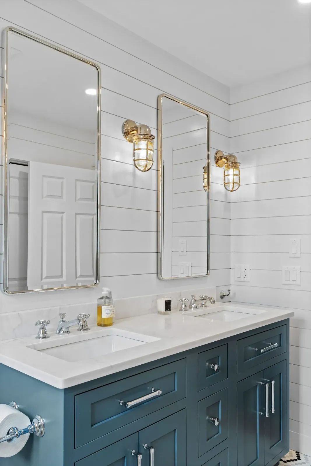 Elegant white bathroom vanity with gold mirrors and sconces, navy cabinets, and a sink countertop