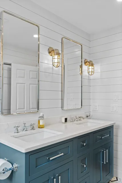 Elegant white bathroom vanity with gold mirrors and sconces, navy cabinets, and a sink countertop