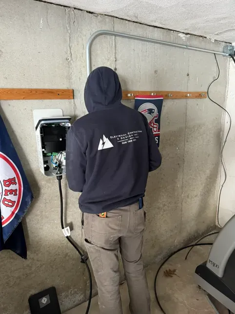 Electrician installing EV charger on white wall; blue vest, tools.