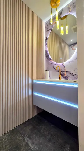 Modern vanity area with striped walls, round mirror, blue LED-lit counter, and dark floor tiles.