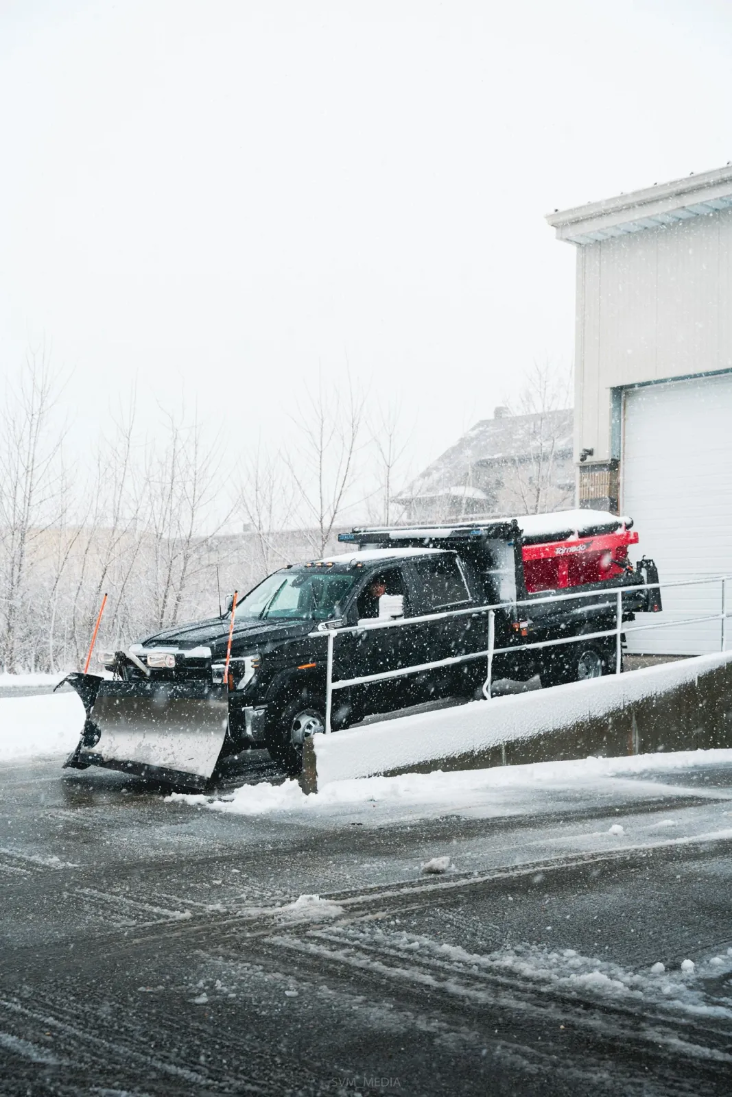 A snow plow truck clearing snow from a driveway during a snowstorm.