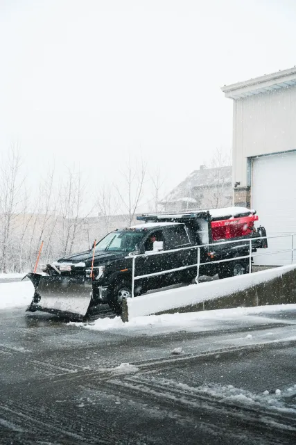 A snow plow truck clearing snow from a driveway during a snowstorm.