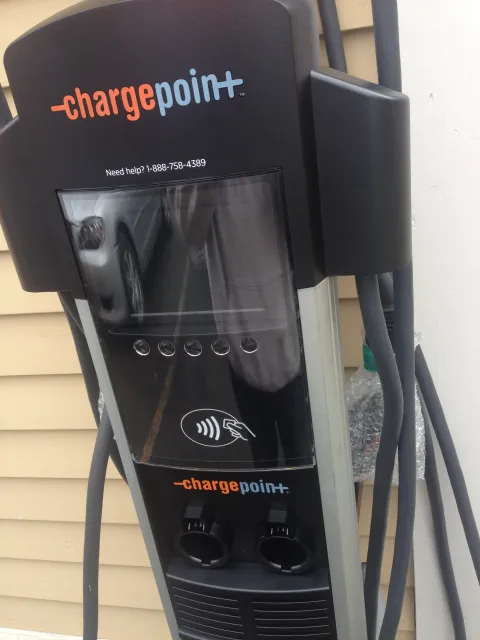 Electric vehicle charging station with a black cover, clear display screen, and two charging ports, labeled 'charge point'.