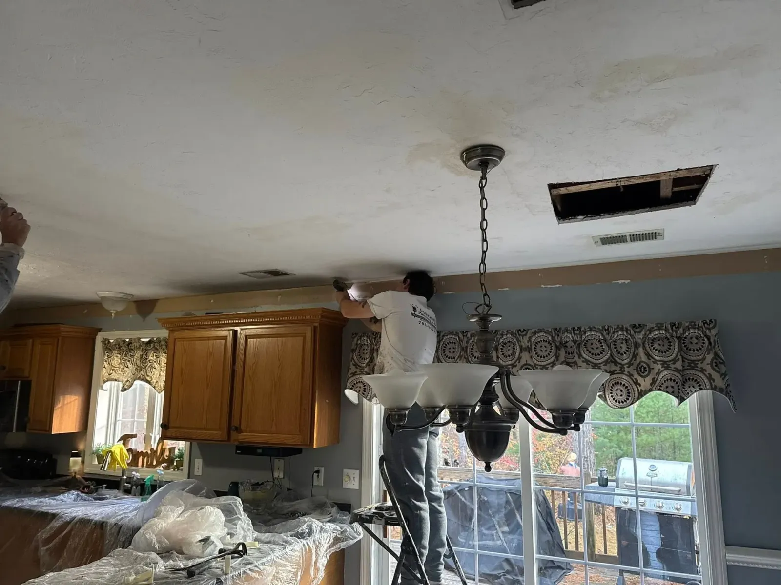 Person working on a kitchen ceiling next to a hanging light fixture and open vent hole