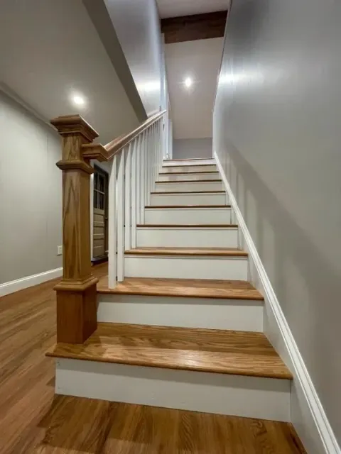 Indoor staircase with wood steps, white walls, and a wooden banister viewed from the bottom.