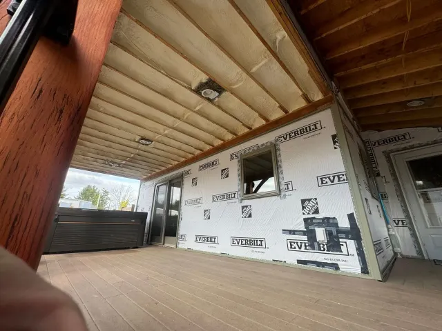 Partially built patio with exposed roof beams, white wall wrapping, and a small window opening