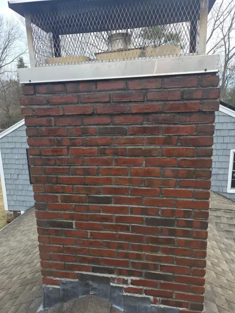 Brick chimney with a metal cap and white trim on a shingled roof, viewed from outside.