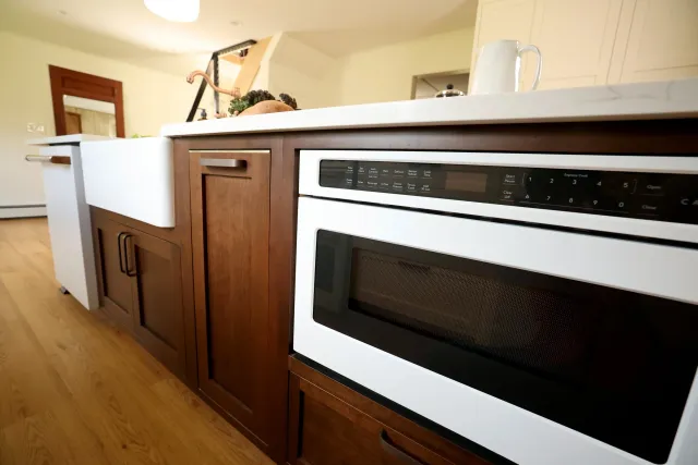 Modern kitchen with wood cabinets, a white oven, and a beige countertop with a white mug and some vegetables on it.