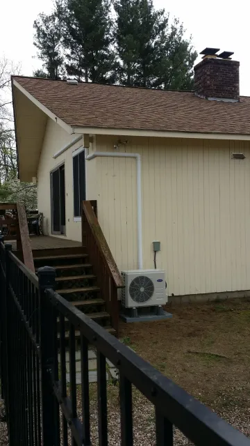 A yellow house with brown roof and a wooden deck, black railing, and outdoor AC unit.