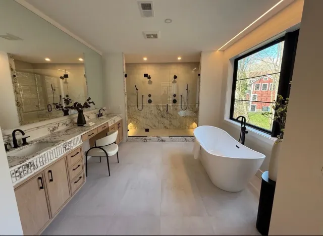 Modern bathroom with a large window, freestanding bathtub, marble vanity with two sinks, and a walk-in shower with glass walls, dark fixtures, and built-in lighting.