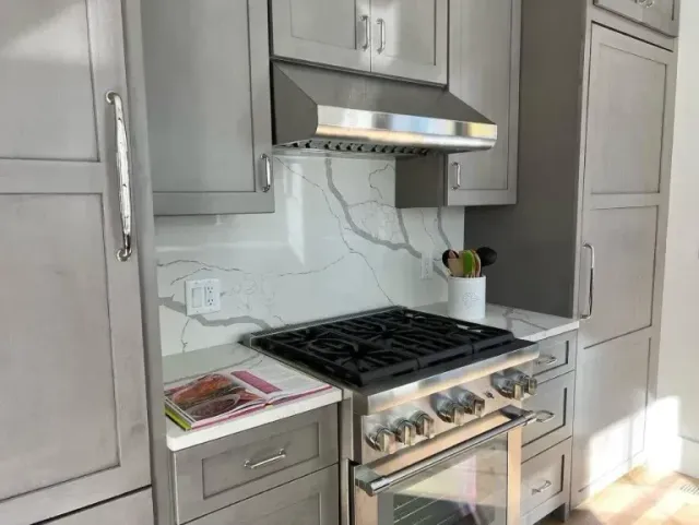 Modern kitchen with stainless steel range, hood, marble backsplash, and light wood cabinets