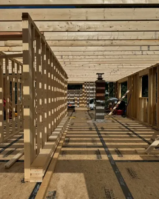 Sunlit wooden construction interior with beams, partitions, and tools casting striped shadows on the floor.